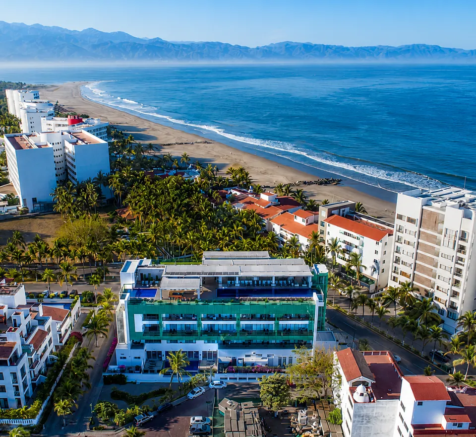 Aerial view of hotel facing beach with palm trees and mountains in the background